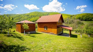 Une cabane en bois avec un toit rouge, entourée de collines verdoyantes et d’arbres.