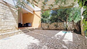 Un espace extérieur aménagé en terrasse, avec un sol en pierre, un coin salon et une structure en forme de pergola.