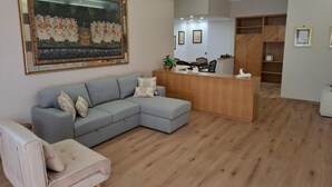 Un salon moderne avec un canapé d’angle gris, un petit fauteuil, un bureau d’accueil en bois et un grand tableau encadré accroché au mur.