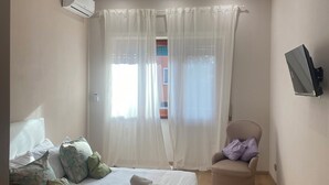 Une chambre à coucher comprenant un lit, des oreillers, une chaise, un appareil de climatisation et un téléviseur.