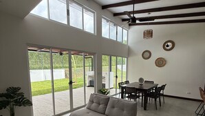 A spacious living area with a sofa, dining table, and chairs. Large windows provide natural light and views of the outdoors. - Casa Kai, a house with everything around it: mountains, beaches, tranquility... (Quebrada Ganado)