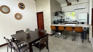 A modern kitchen with a central island, a dining area with a dark wooden table and chairs, and a ceiling fan. - Casa Kai, a house with everything around it: mountains, beaches, tranquility... (Quebrada Ganado)