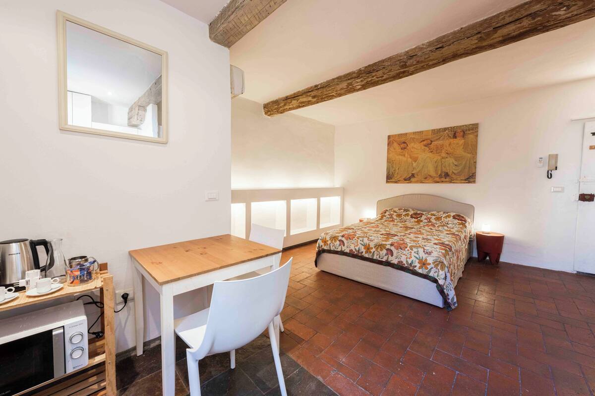 A bedroom with a bed, a wooden desk, a chair, a table, and a painting on the wall.