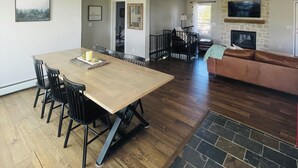 A spacious living area with a wooden dining table, black chairs, a brown sofa, a fireplace, and a stone accent wall. - Cozy Moose Grove: ski, hike, fish & relax (Fairplay)