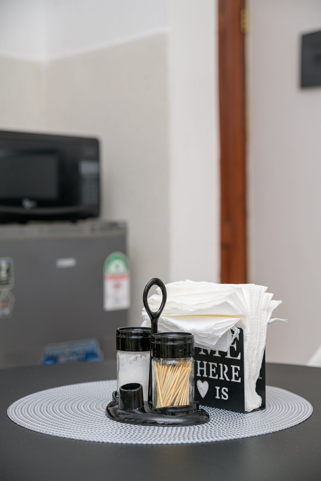 A table with a tissue box, a container with toothpicks, and a small black object on a woven placemat.