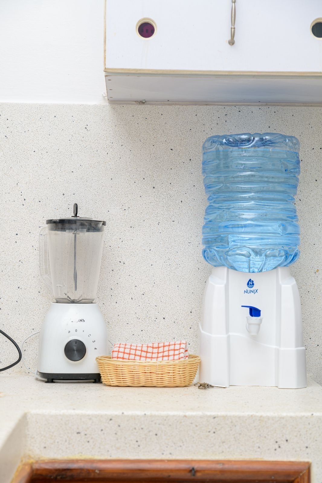 Une cuisine équipée d’un mixeur, d’un distributeur d’eau et d’un panier en osier posé sur le plan de travail.