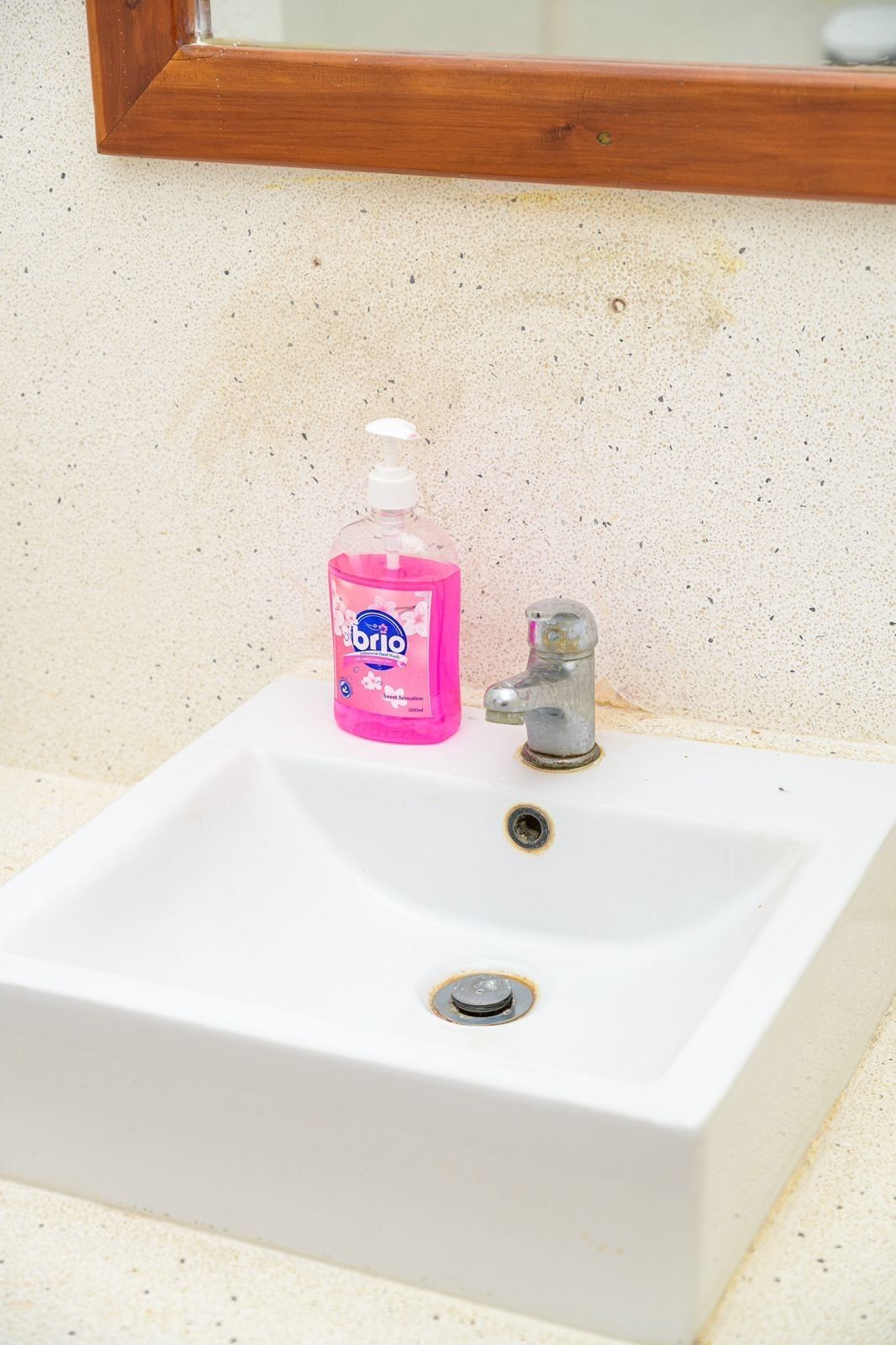 A white bathroom sink with a pink bottle of Brio soap and a silver faucet.