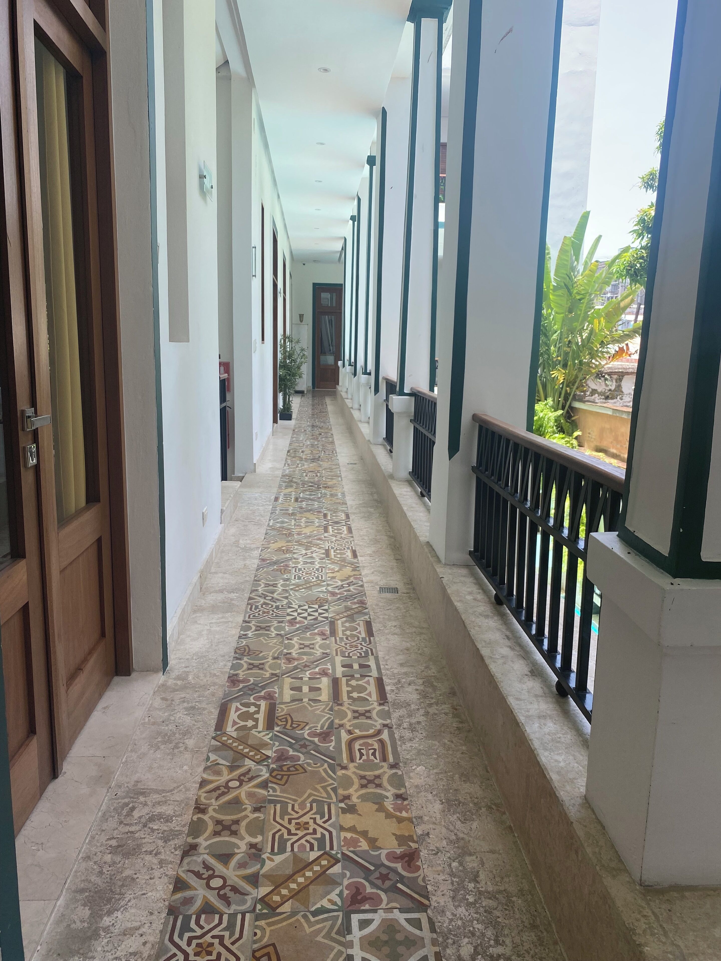 A corridor with patterned flooring, white walls, and a balcony with a railing.