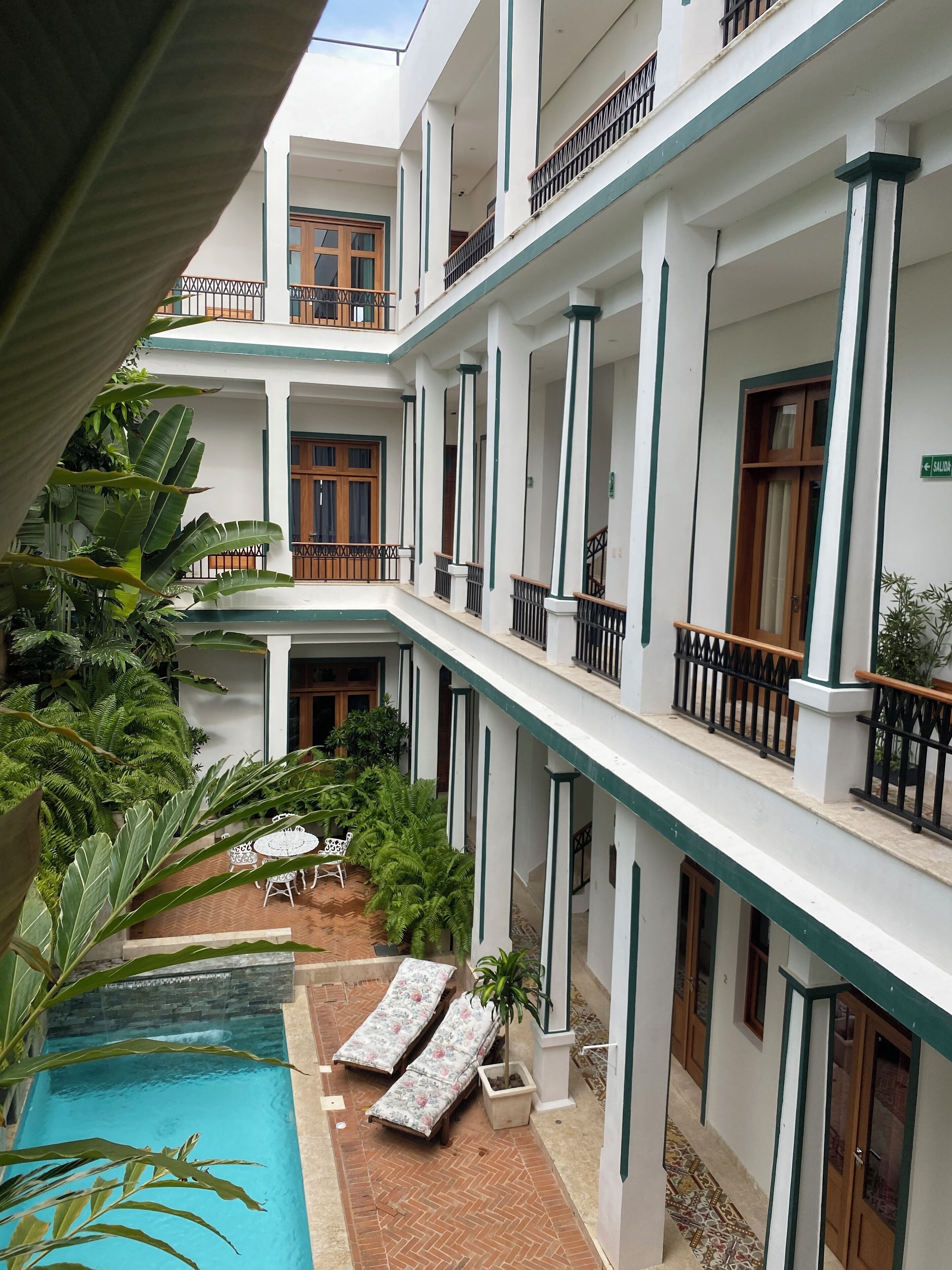 Un edificio de varios pisos con un patio que cuenta con una piscina, sillas de descanso y plantas en macetas.