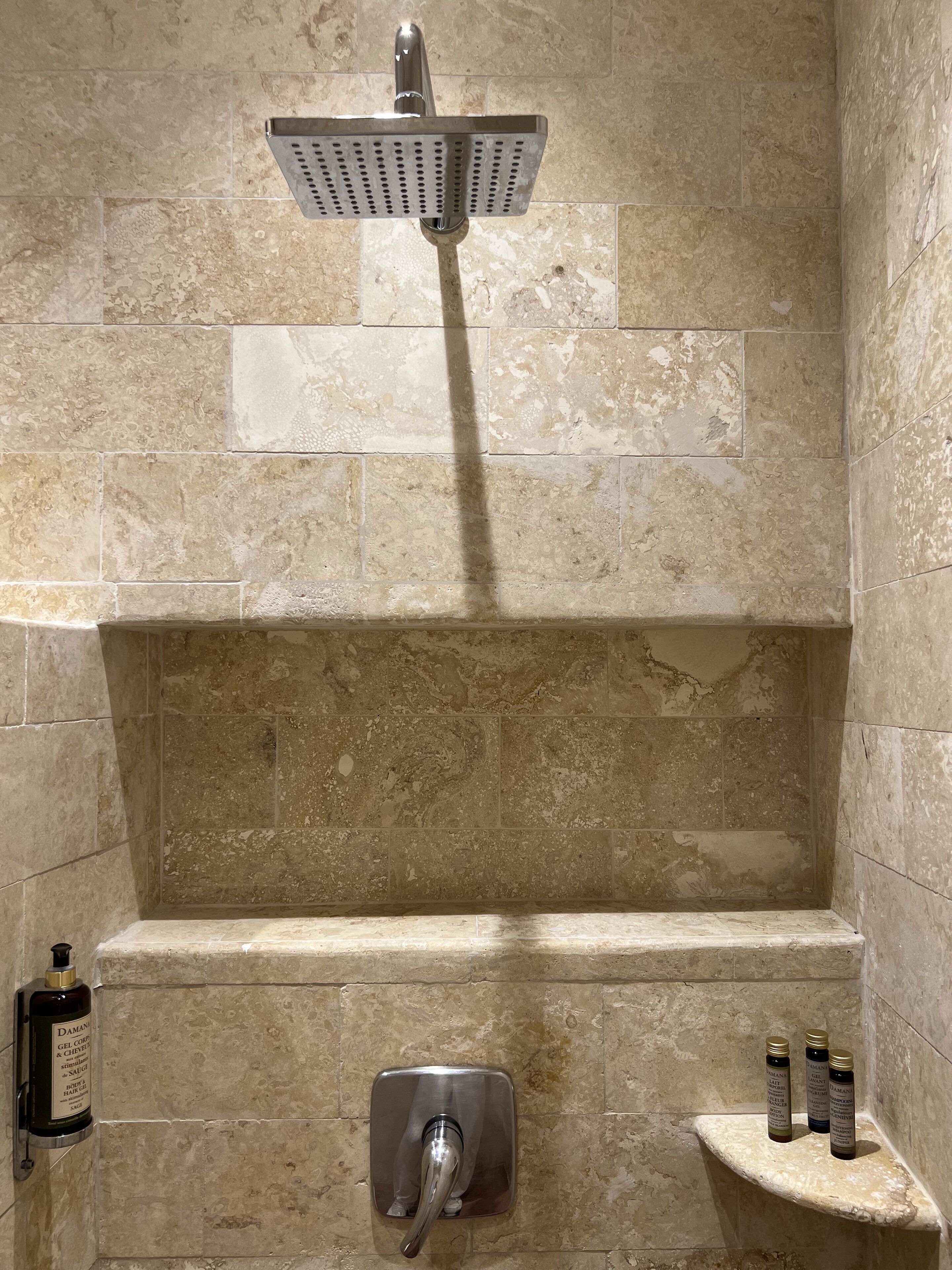 A shower area with a handheld showerhead, a soap dispenser, and three bottles of shampoo on a shelf.