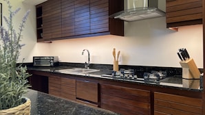 A modern kitchen with dark wooden cabinets, a granite countertop, a built-in oven, and a stainless steel sink. - Boutique Hotel Casa Grande, Dominican Voyage Familiar Suite, 2 BR (Santo Domingo)