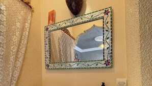 Un bagno con un lavandino in mosaico originale, uno specchio decorativo e una parete in pietra.