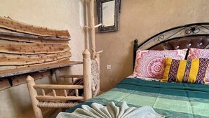 Una stanza con un letto, una sedia in legno, un cesto di vimini e uno specchio a muro.