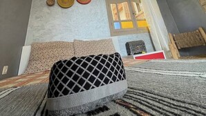 Una stanza con soffitto grigio, un lampadario a sospensione, un letto con coperta fantasia, una parete con cesti intrecciati e un muro in pietra con una finestra.