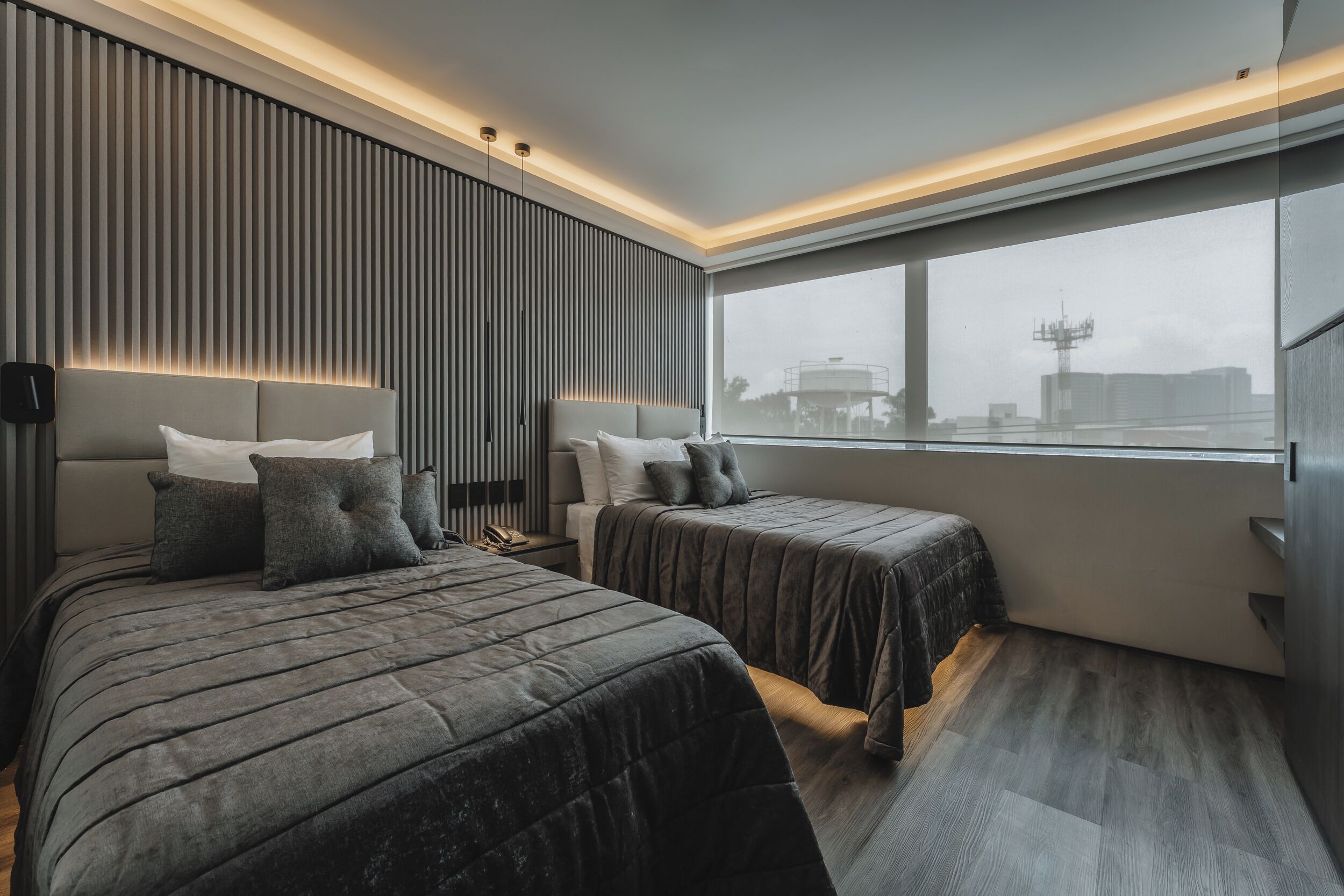 Una habitación de hotel moderna con dos camas, un ventanal grande y vistas a la ciudad.
