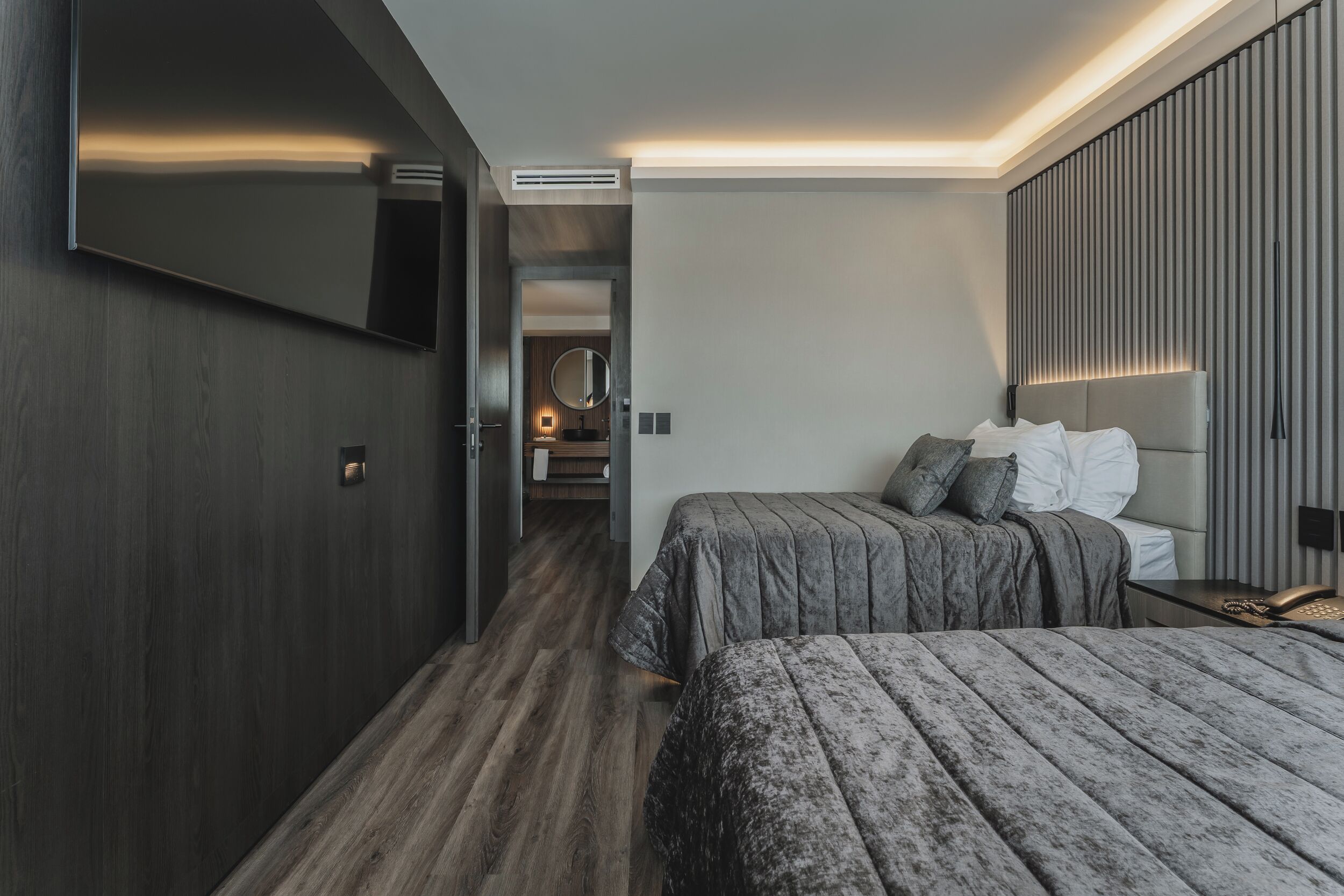 A modern hotel room with a large bed, a smaller bed, a TV, and a bathroom visible through an open door.
