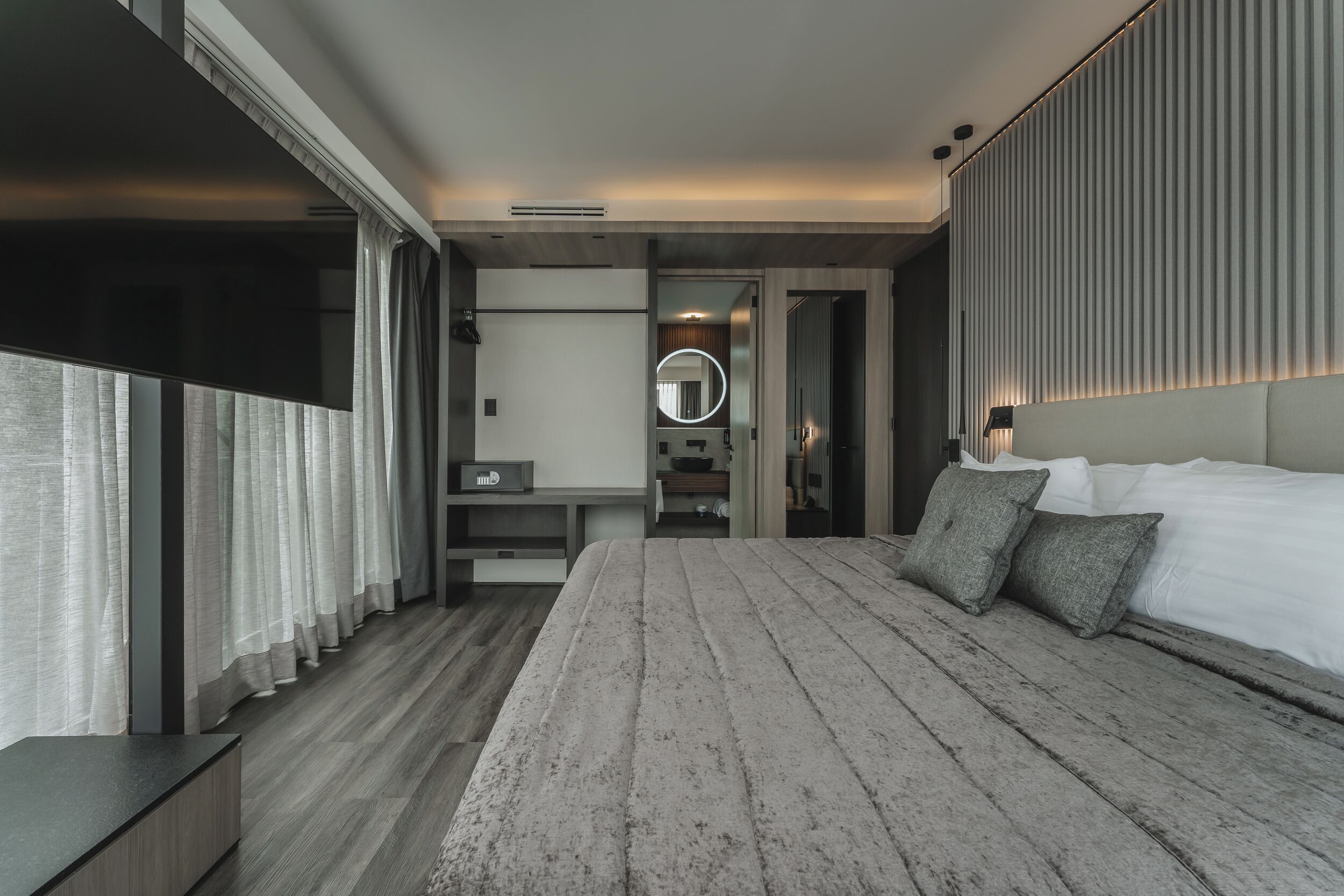 A modern hotel room with a large bed, a bedside table, a mirror, and a view of the city.