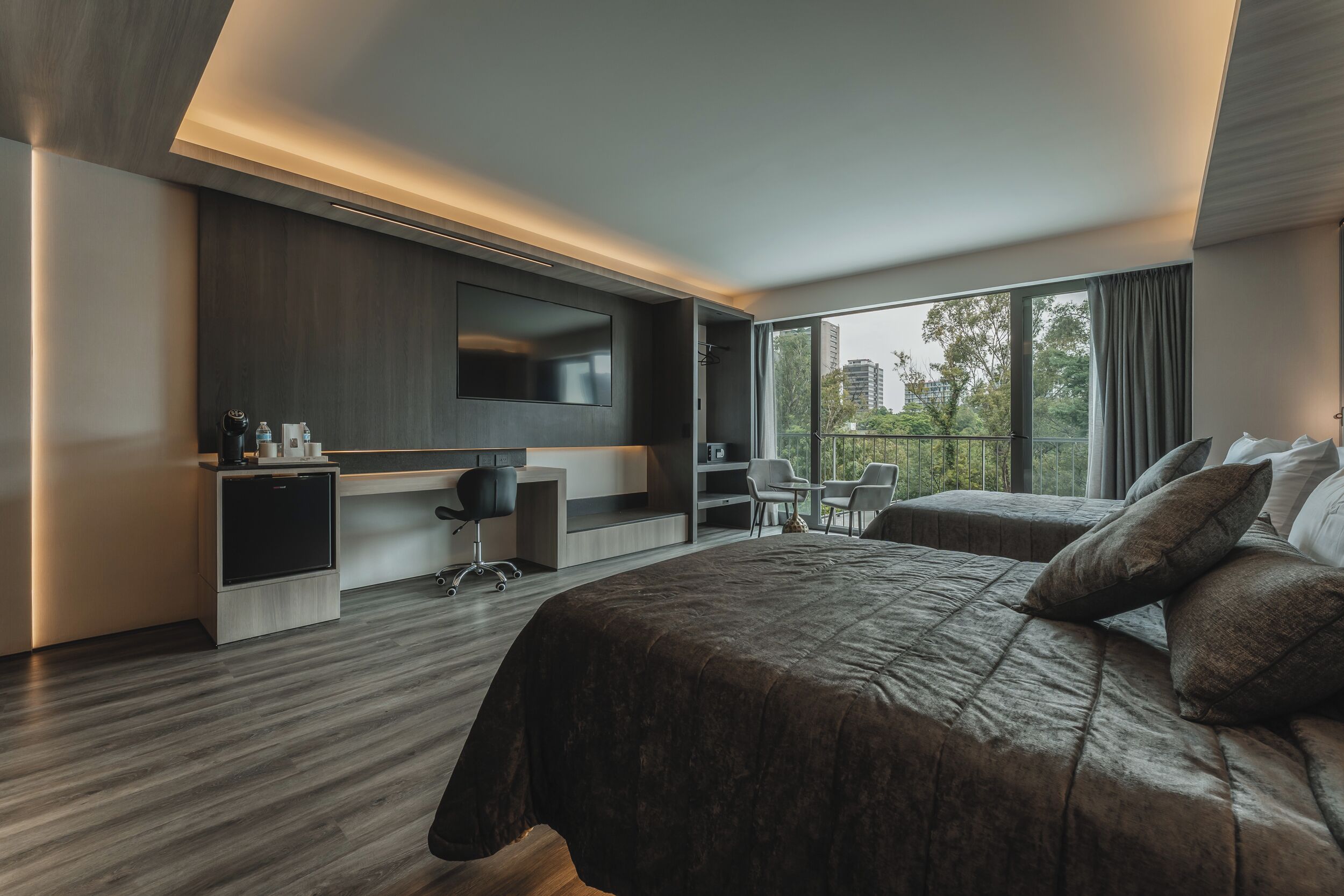 Una habitación de hotel moderna con una cama grande, un escritorio con silla, un televisor y un balcón con vista a la ciudad.