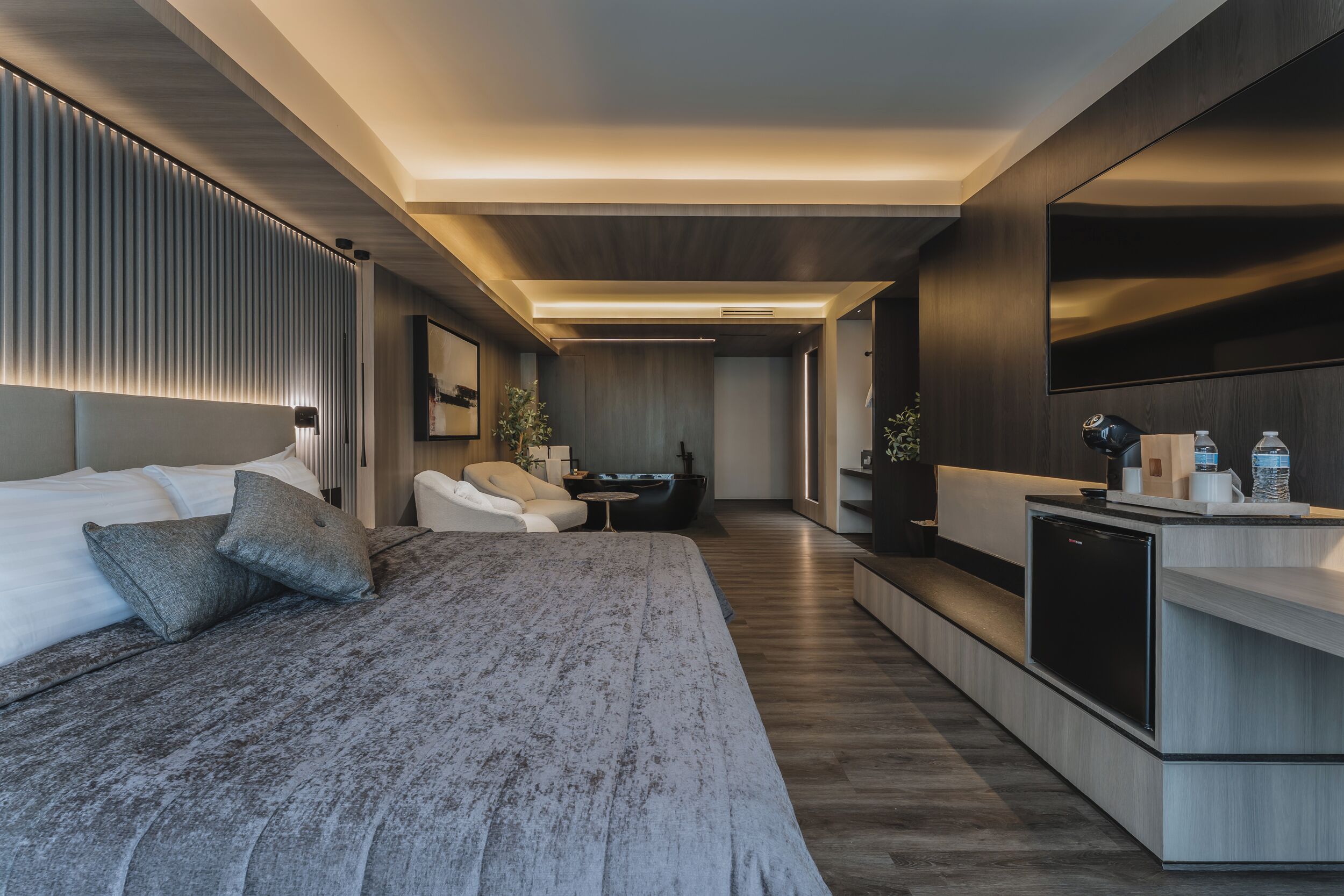 Ein modernes Hotelzimmer mit einem großen Bett, einer Sitzecke, einer kleinen Küche und einem Fernseher.