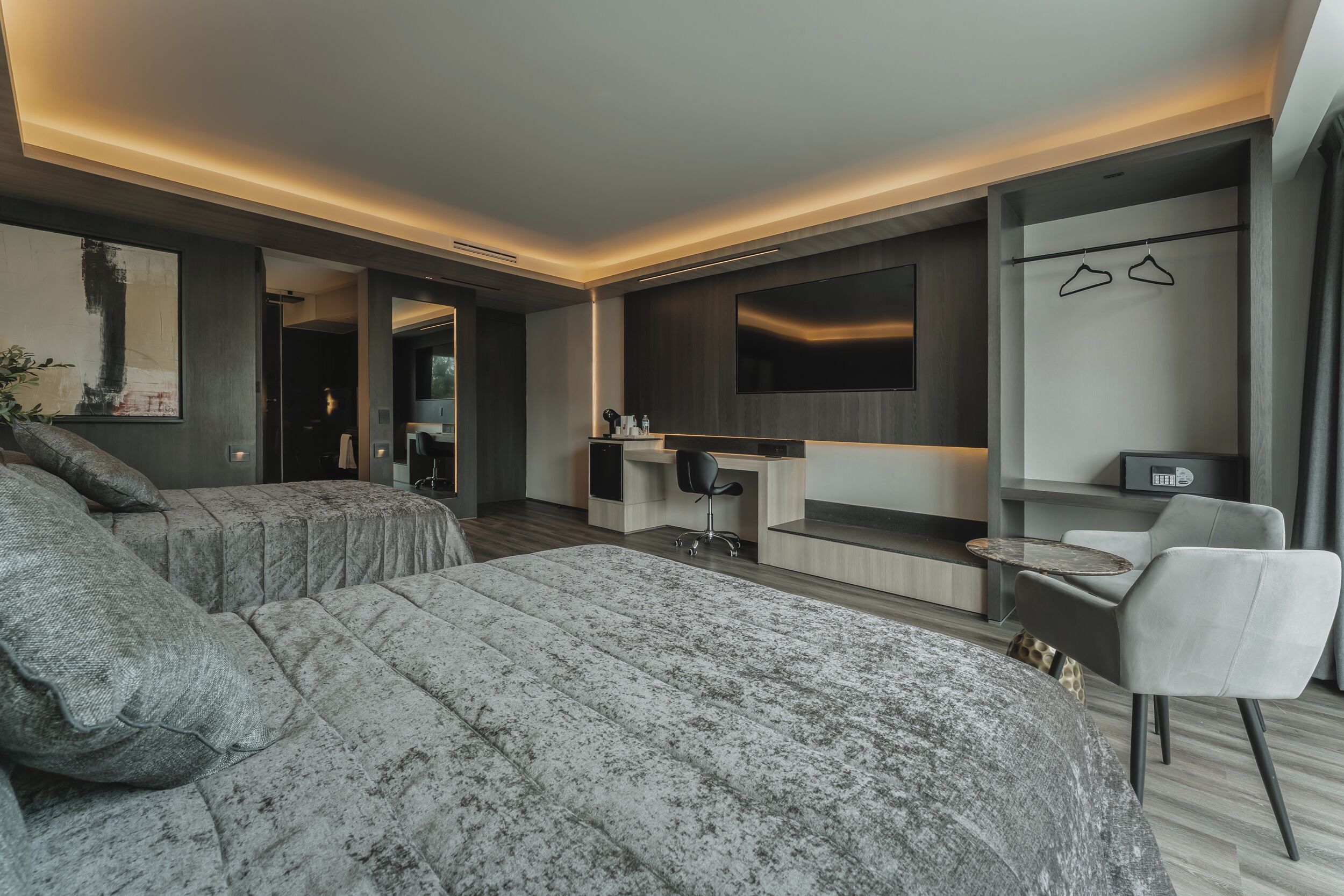 A modern hotel room with a large bed, a desk, a chair, a TV, and a wardrobe.