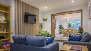 Un salon moderne comprenant un canapé, une table basse, une bibliothèque, un téléviseur et un coin repas avec une table et des chaises.