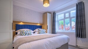 Une chambre à coucher avec un grand lit, une tête de lit dotée d’un éclairage intégré, une fenêtre avec des rideaux et un radiateur.