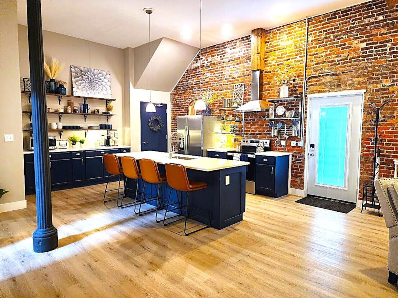 Una cocina moderna con pared de ladrillo, suelo de madera, una isla central con taburetes de bar y un ventanal grande.