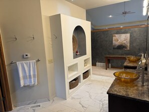 A bathroom with a large mirror, two vessel sinks, a towel rack, and a ceiling fan.