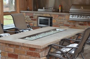 An outdoor patio with a stone fireplace, a built-in microwave, and a gas grill.