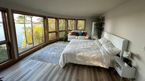 Un dormitorio moderno con una cama grande, una mesita de noche y vistas a un lago a través de amplios ventanales.