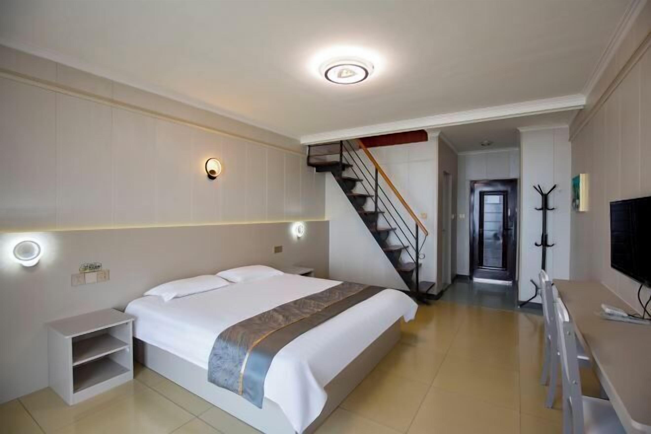 Une chambre d’hôtel comprenant un lit, des tables de chevet, un bureau, une chaise, un escalier et un porte-manteau.