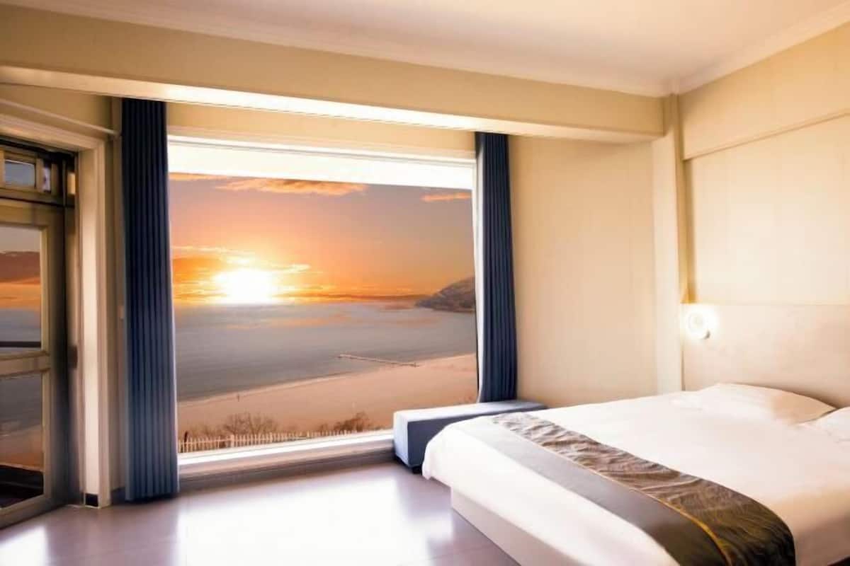 A hotel room with a large window offering a sunset view over a body of water.