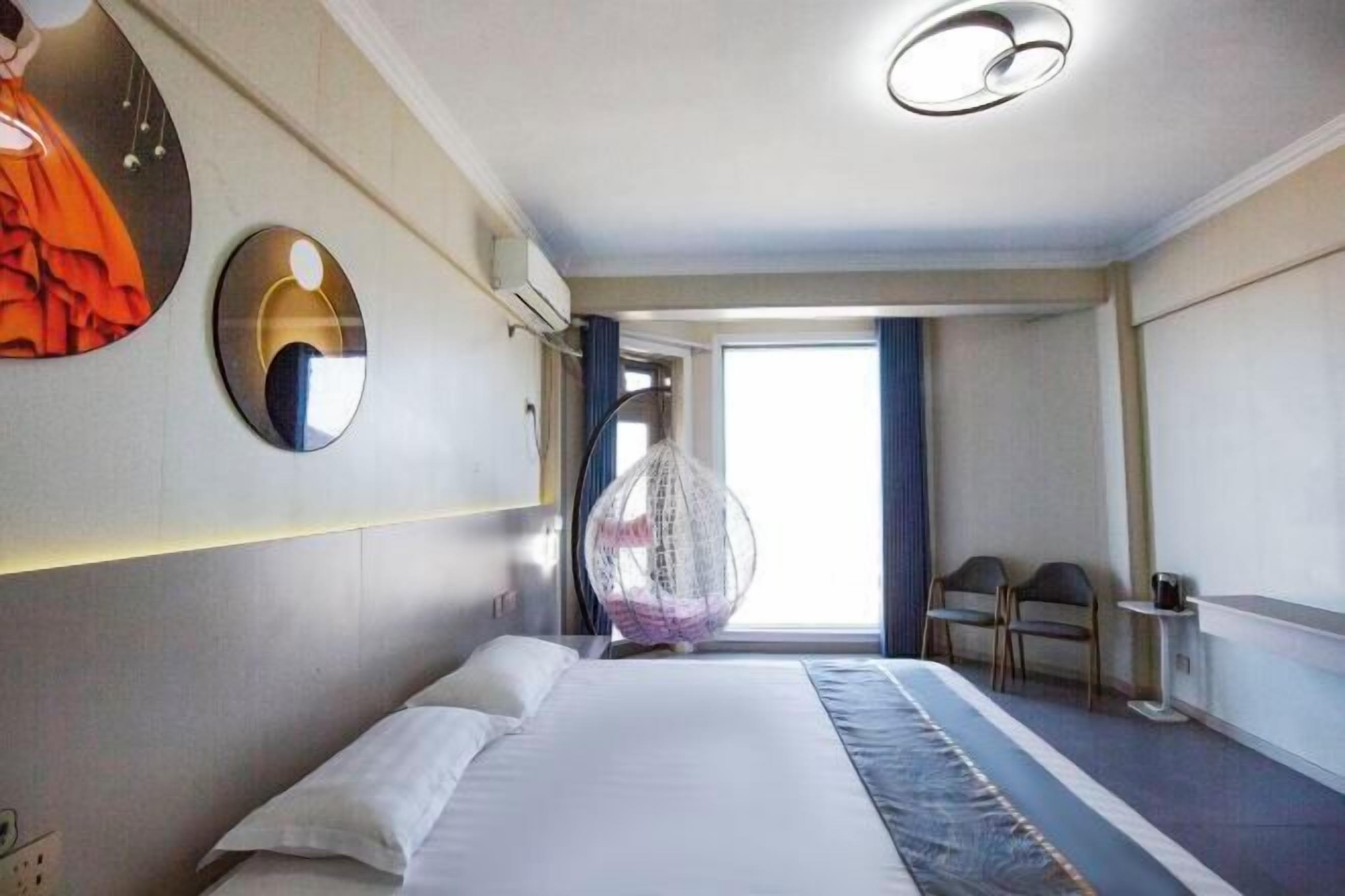 Une chambre d’hôtel avec un lit, un fauteuil suspendu, un miroir et une fenêtre.
