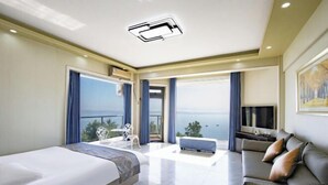 Quarto de hotel moderno com uma cama grande, sofá, televisão e varanda com vista para o mar.