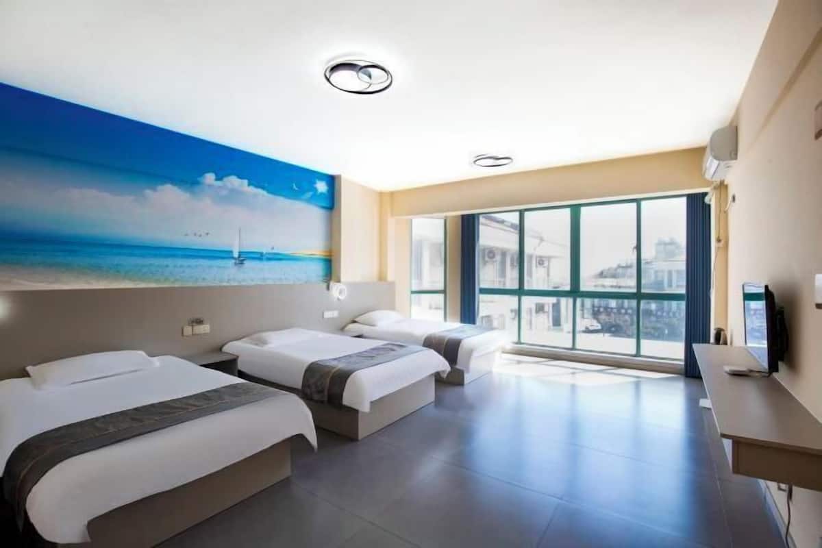 A hotel room with two beds, a large window with a city view, and a painting of a beach scene.