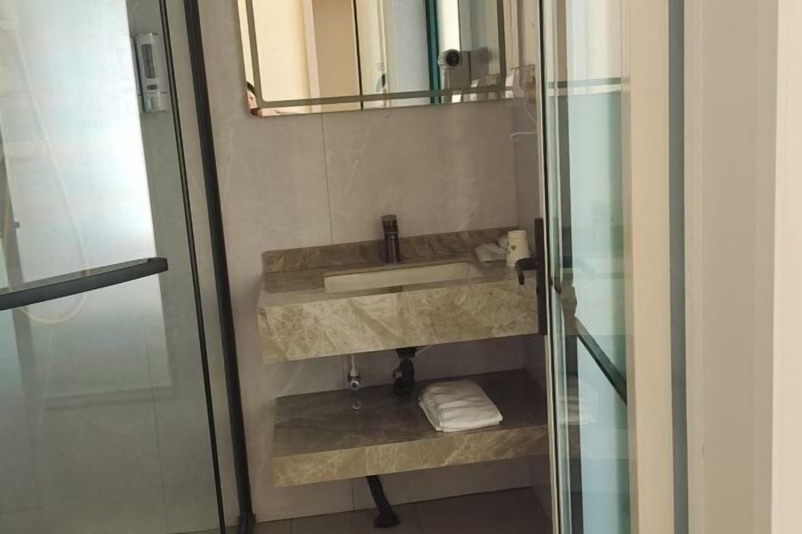 A bathroom with a glass door, a sink with a mirror above it, and a towel on the counter.