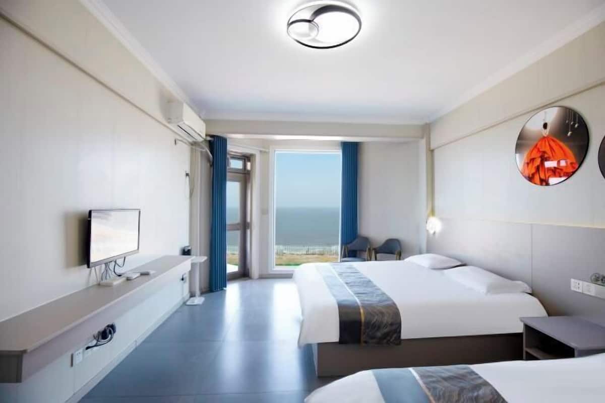 A hotel room with a bed, a TV, a desk, and a view of the ocean.
