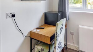A small room with a wooden desk, a television on a stand, a remote control, and a window with curtains. - 1 bedroom accommodation in Walcott (Walcott)