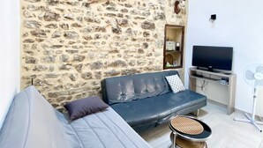 Una sala de estar con pared de piedra, un sofá, un televisor y un ventilador.