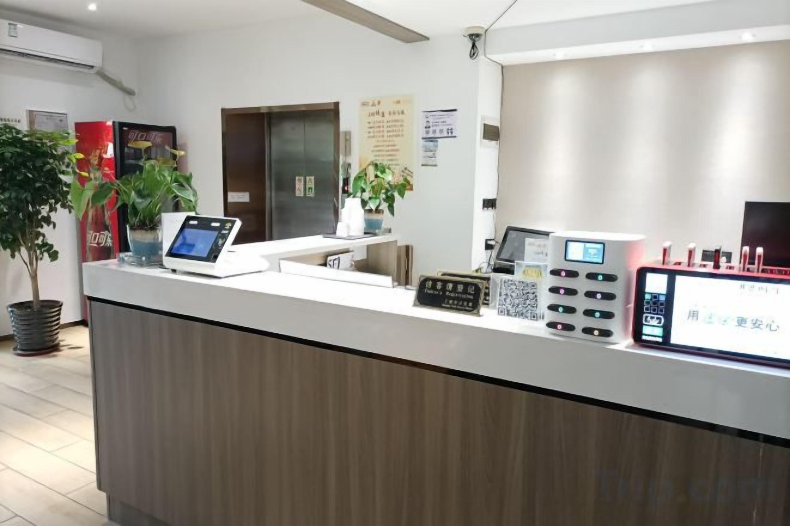 A reception desk with a digital screen, a plant, and a QR code scanner.