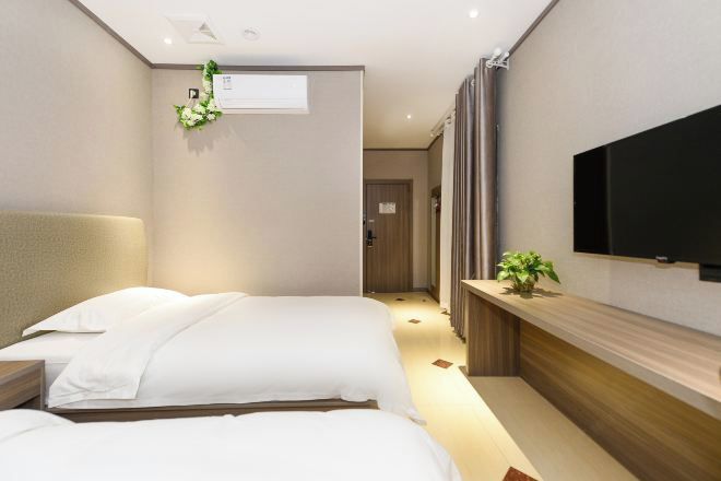 A hotel room with two beds, a TV, a plant, and a wooden console.