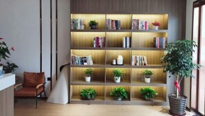 A modern living room with a wooden bookshelf, a brown leather chair, and potted plants. - Jizhu Auto Business Hotel (Shanghai)