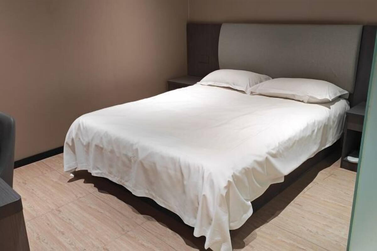 Un letto rifatto con una coperta bianca e cuscini, un pavimento in legno e una testiera scura.