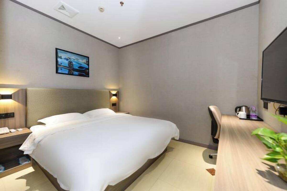 Una camera d'albergo con un letto, comodino, lampada, televisore e una scrivania con una sedia.