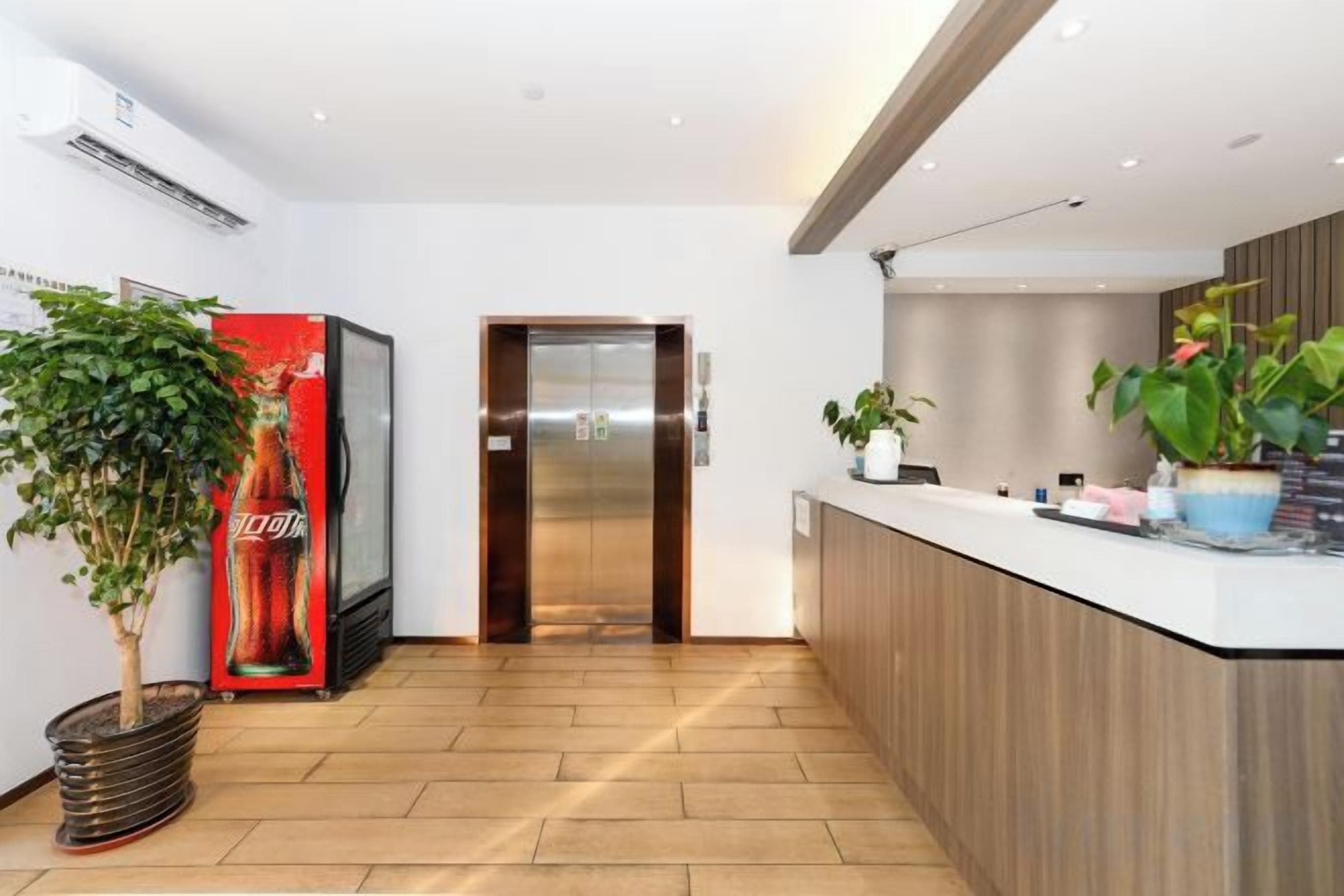 A modern reception area with a Coca-Cola refrigerator, an elevator, and a reception desk with potted plants.