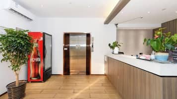A modern reception area with a Coca-Cola refrigerator, an elevator, and a reception desk with potted plants.