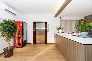 A modern reception area with a Coca-Cola refrigerator, an elevator, and a reception desk with potted plants. - Jizhu Auto Business Hotel (Shanghai)