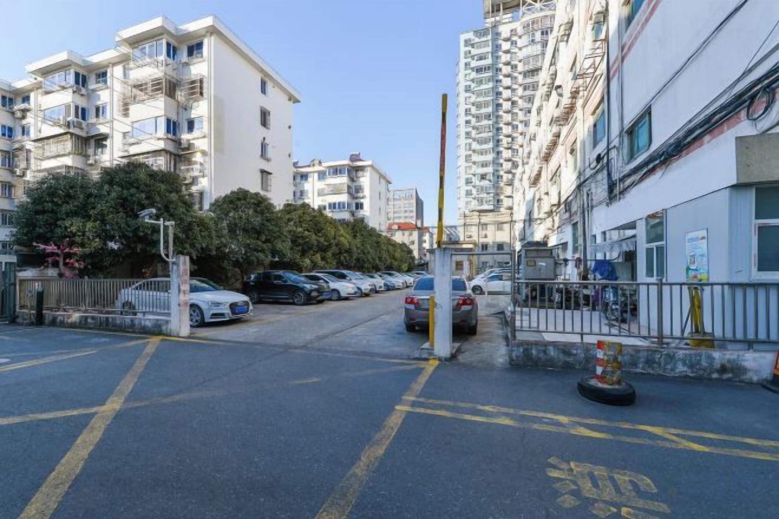 A residential street with parked cars, a gated entrance, and multi-story buildings.