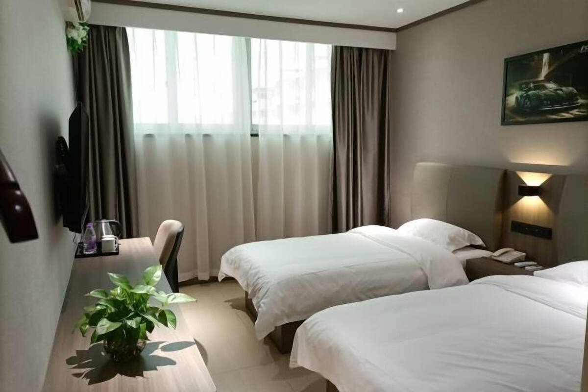 Una camera d'albergo con due letti, una scrivania con una pianta, una televisione e un quadro appeso al muro.