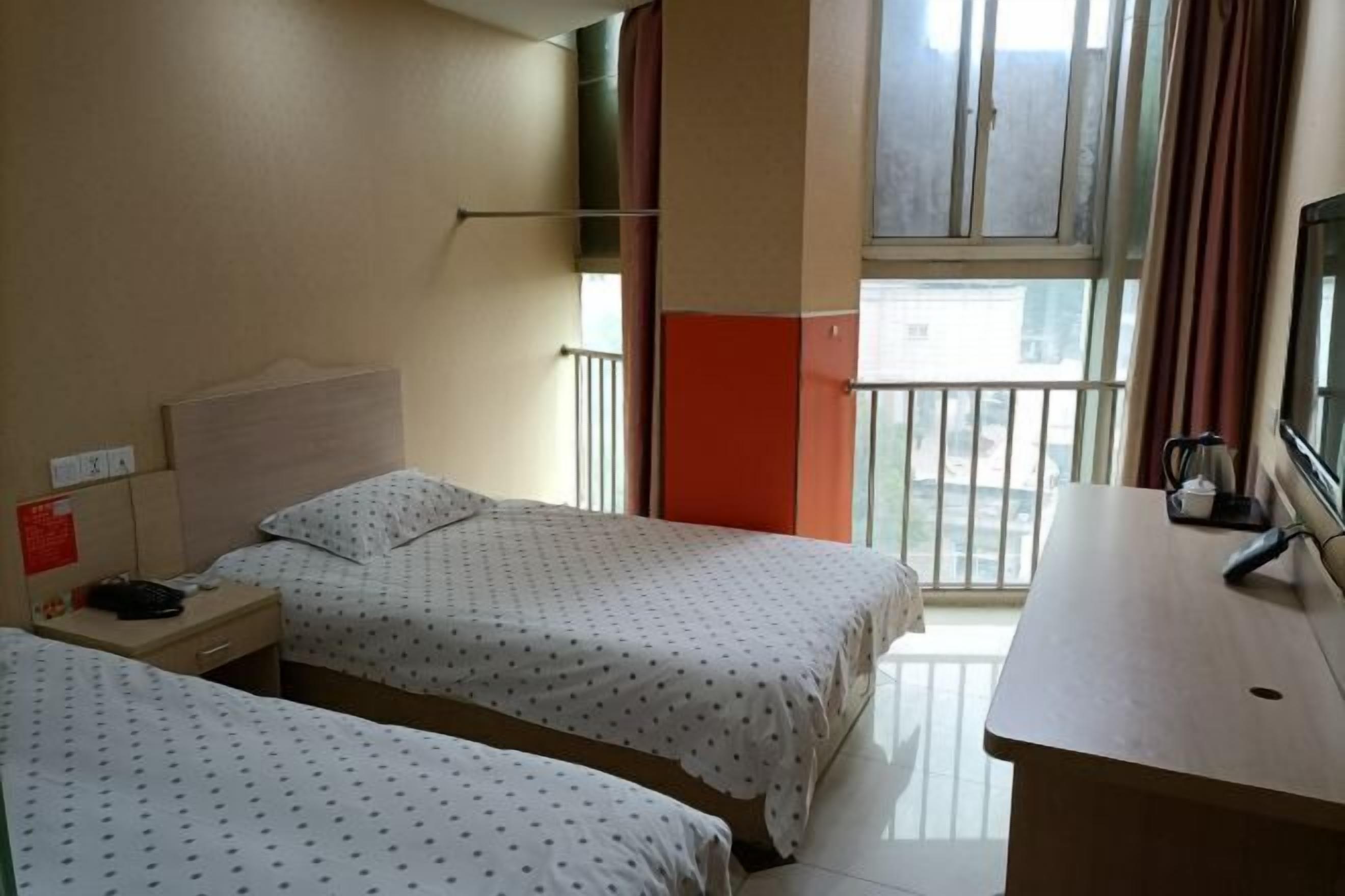 A hotel room with two beds, a desk, a window with a view, and a balcony.